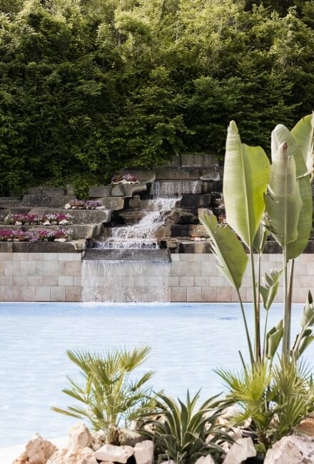 Piscina del resort con cascata, piante tropicali e alberi verdi.