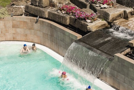 Piscina con cascata, persone in acqua, parete curva.