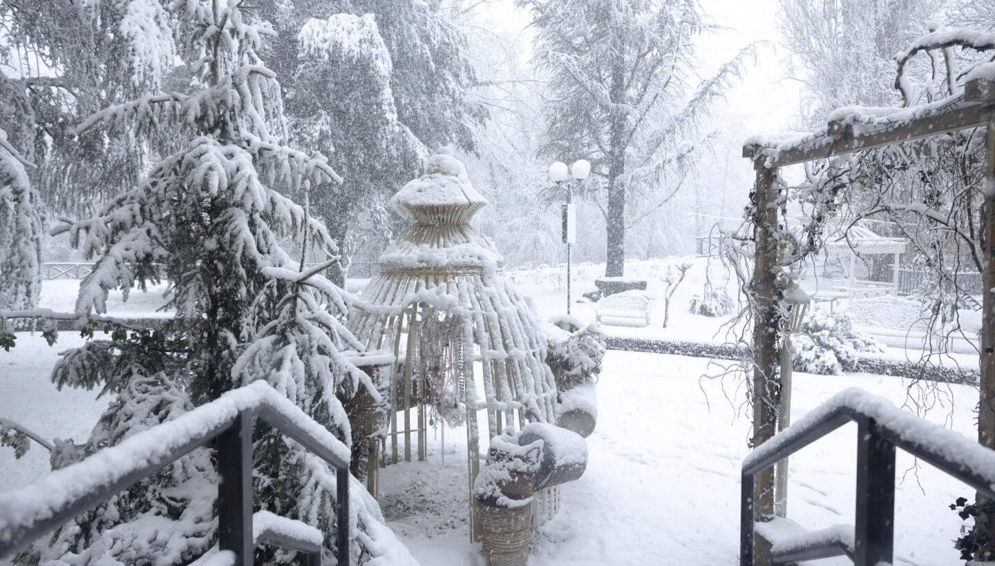 Parco innevato con gazebo, alberi e lampione sullo sfondo.