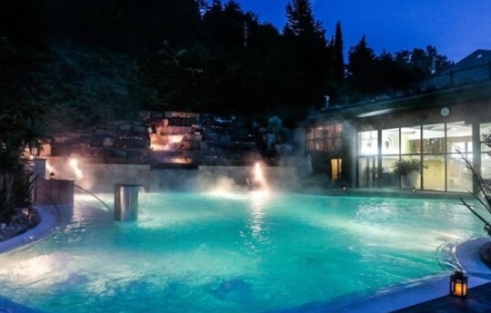Piscina illuminata al crepuscolo con acqua turchese e vapore.