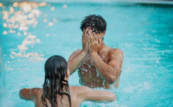 Due persone in una piscina, una sommersa con le mani sul viso.