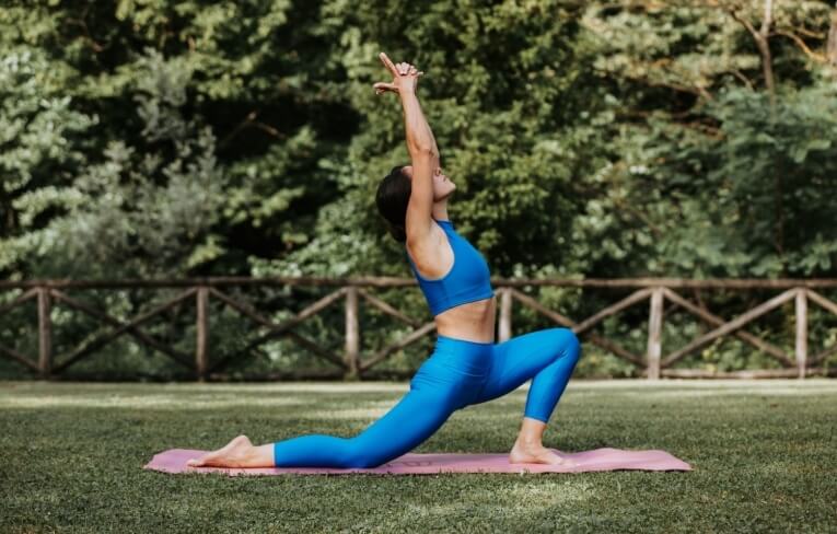 Persona che pratica yoga su un tappetino rosa in un'area verde.