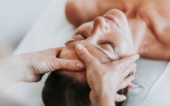 Una persona riceve un massaggio al viso con gli occhi chiusi.