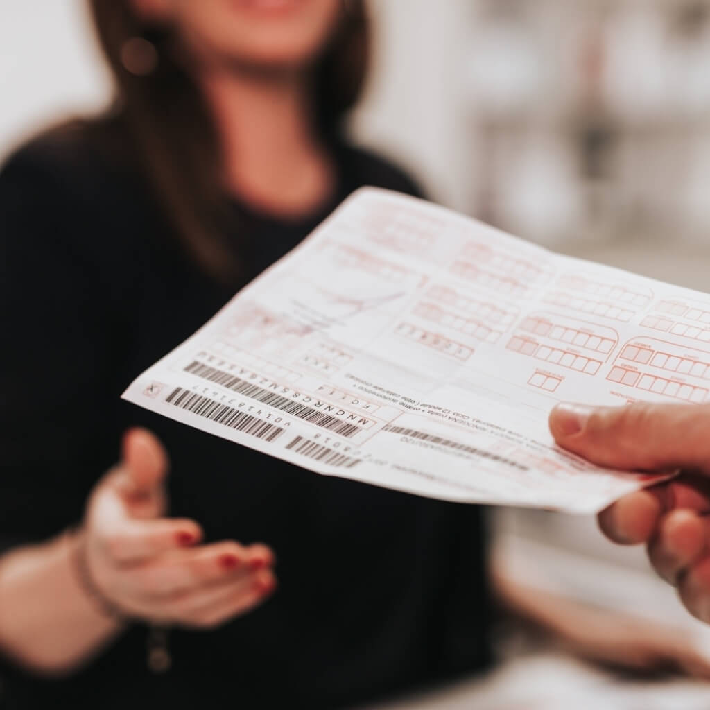 Una mano tiene un documento bianco con testo rosso e codice a barre.