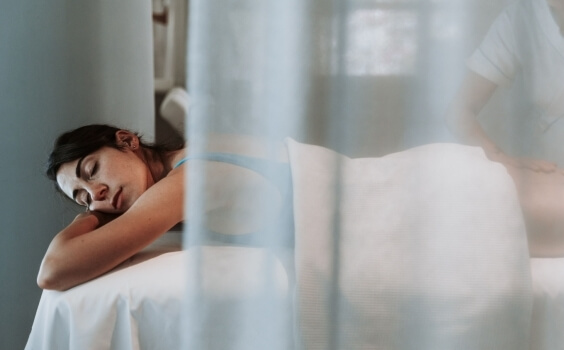 Una donna su un tavolo da massaggio, con un massaggiatore parzialmente visibile.