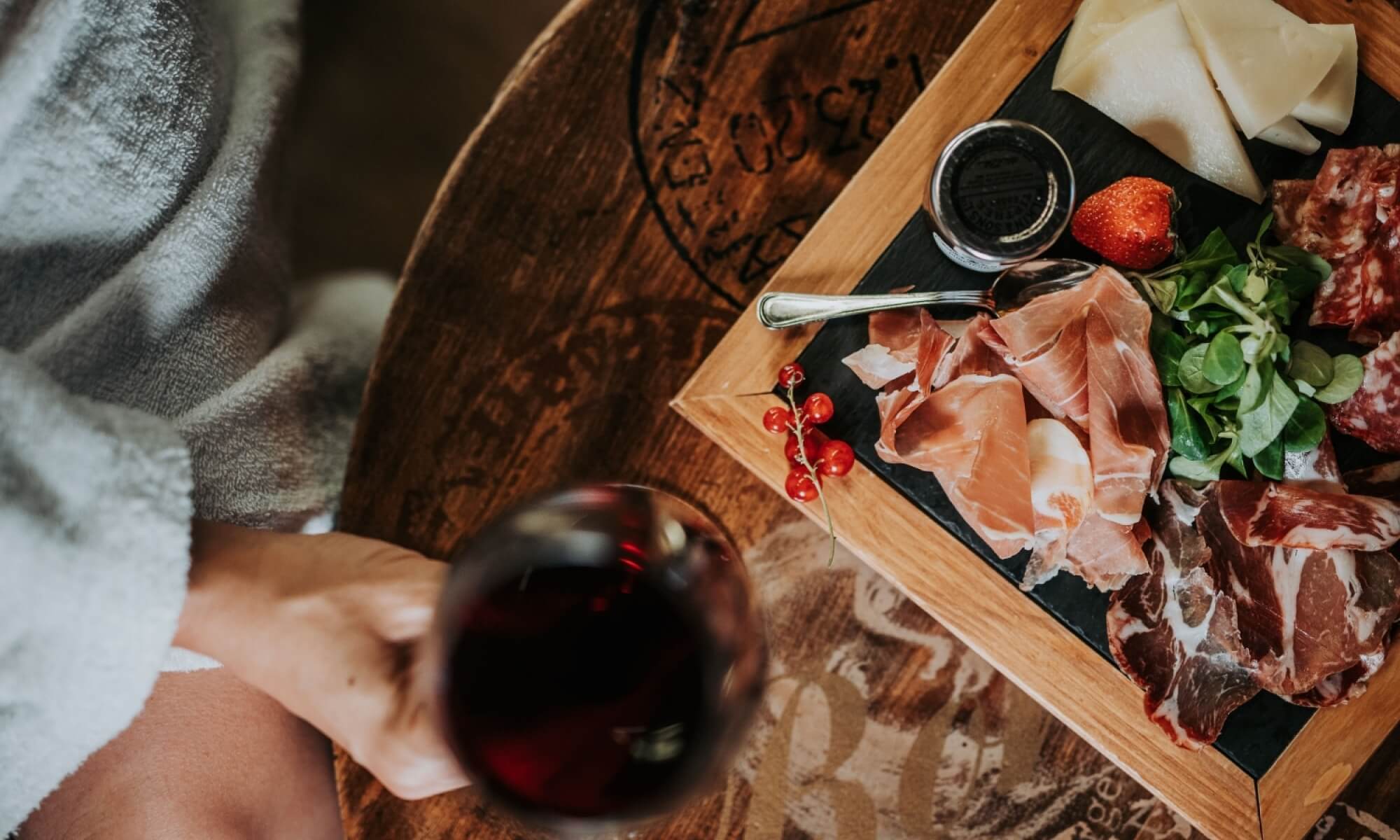 Tagliere di salumi e formaggi con vino rosso e frutta.