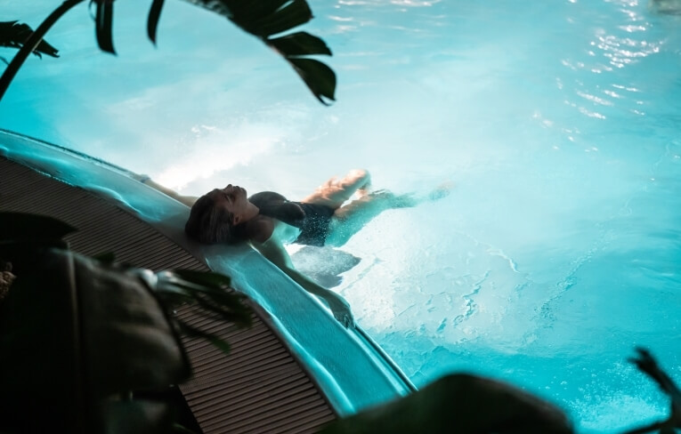 Persona che galleggia in una piscina turchese circondata da palme.