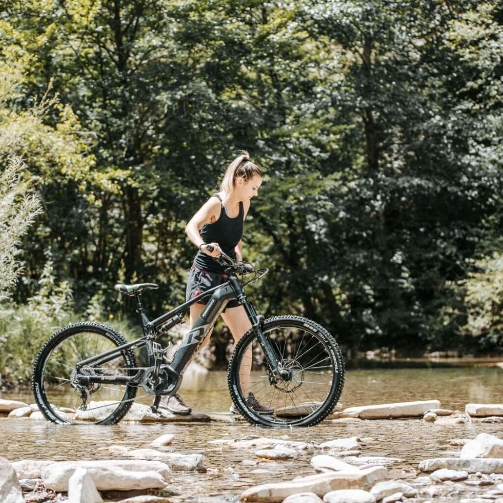 Donna con bicicletta attraversa un torrente roccioso.