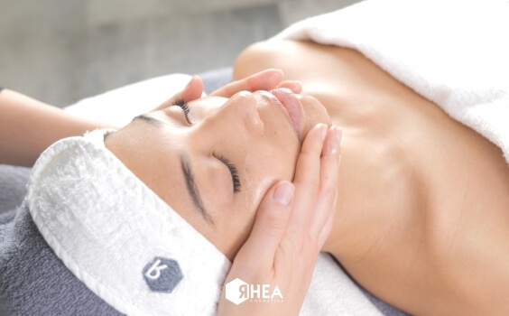 Person receives a facial massage with Rhea Cosmetics logo visible.   Eine Person erhält eine Gesichtsbehandlung mit Rhea Cosmetics-Logo.