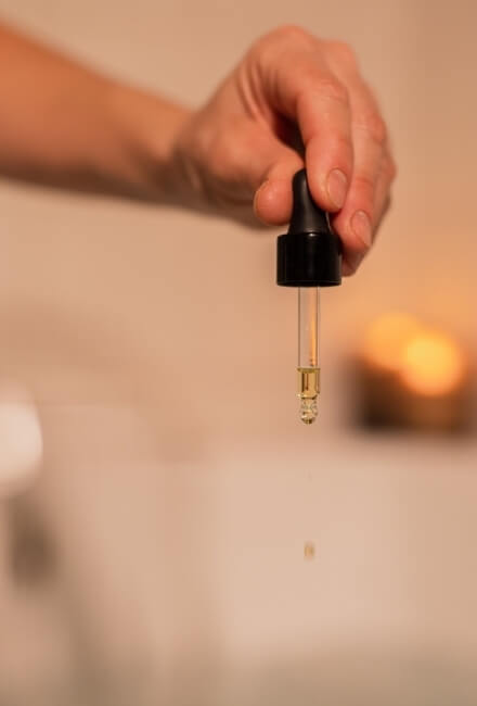 Mano con pipetta che rilascia un liquido dorato in un ambiente luminoso.