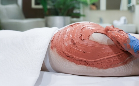 Persona con maschera di argilla rossa su gamba e glutei.