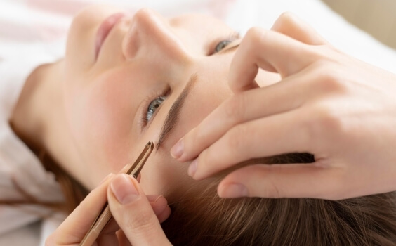 Person's face in profile, someone shaping eyebrow with tweezers.   Gesicht im Profil, jemand formt Augenbraue mit Pinzette.
