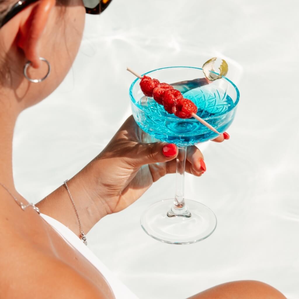 Persona con un drink blu e frutti rossi su uno stecchino.