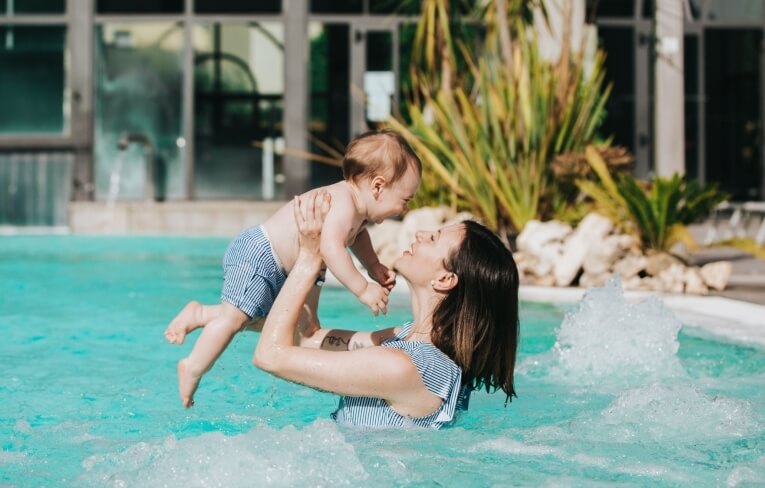 Donna con un bambino in piscina, entrambi indossano abiti a righe.