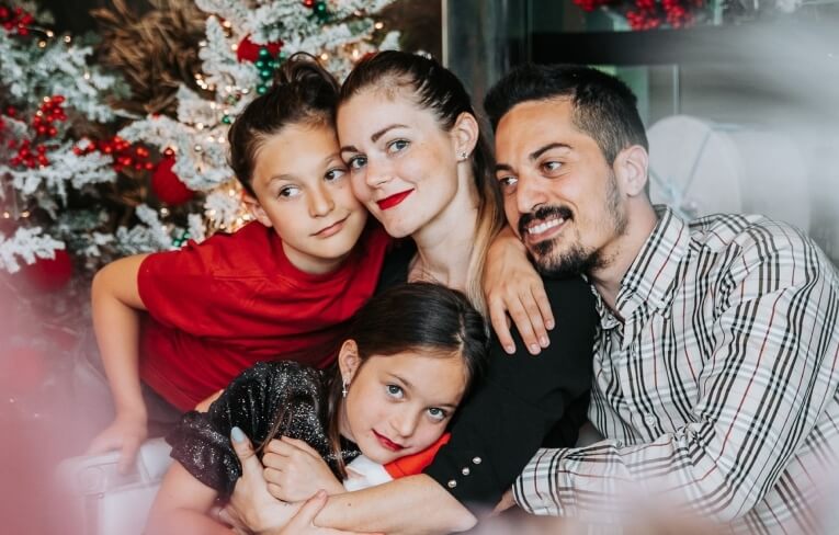 Una famiglia di quattro persone davanti a un albero di Natale decorato.