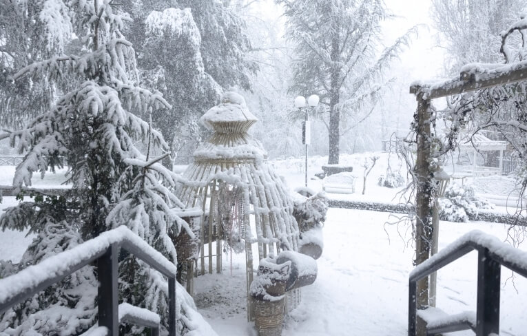 Gazebo decorativo coperto di neve con alberi e lampione sullo sfondo.