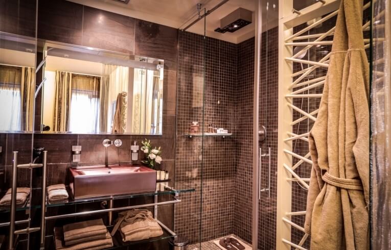Bagno d'hotel con doccia in vetro, lavabo in rame e accappatoio.