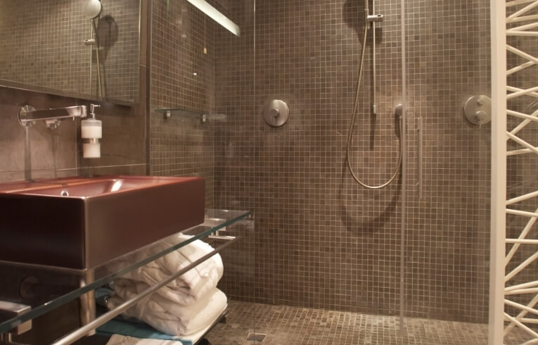 Bagno moderno con piastrelle marroni, doccia a filo e lavabo.