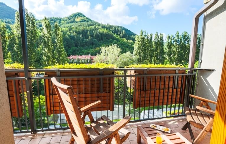 Balcone con sedie, tavolo, succo d'arancia e vista montana.