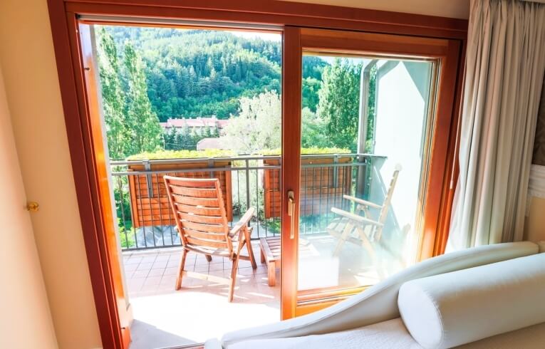 Camera d'hotel con balcone, sedie in legno e vista collinare.