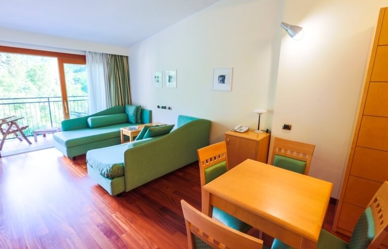 Camera d'hotel con chaise longue verdi e balcone arredato.