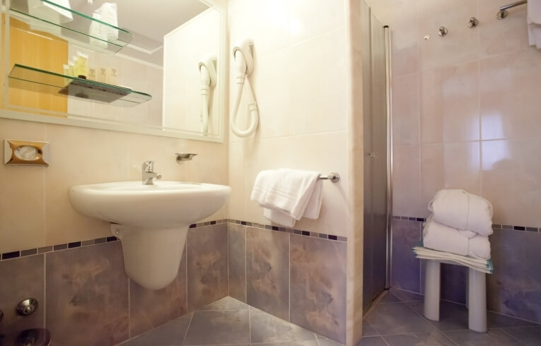 Bagno d'hotel con lavabo, specchio, doccia e asciugamani piegati.