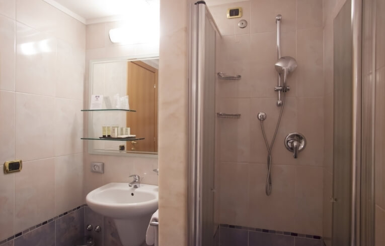 Bagno d'hotel con lavabo, specchio, scaffali e doccia.
