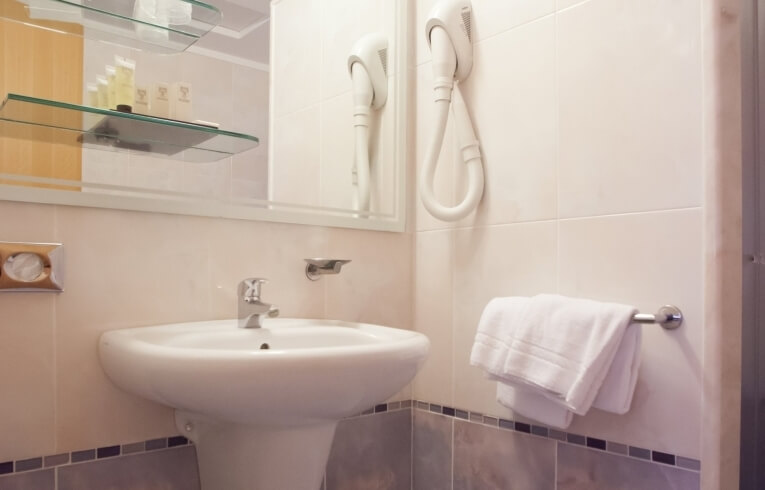 Lavabo con rubinetto cromato, specchio, asciugamano e asciugacapelli.