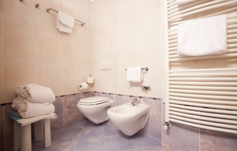 Bagno con bidet, wc, asciugamani piegati e piastrelle chiare.