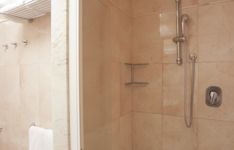 Light-tiled shower stall with silver fixtures and towel hooks.