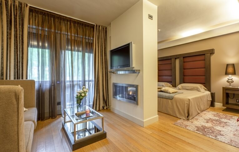 Camera d'hotel con letto, divano, TV e camino.