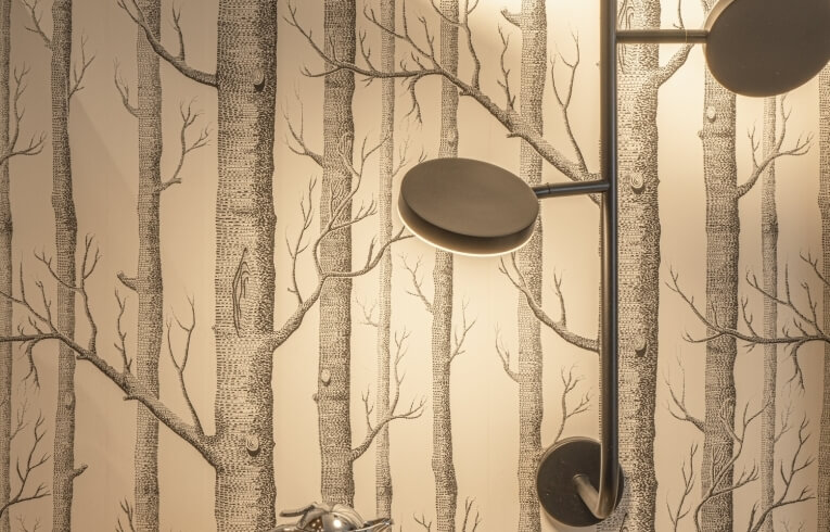 Wall with tree-patterned wallpaper and illuminated metal lamp.