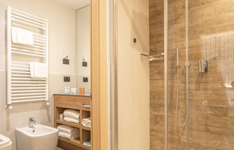 Hotel bathroom with bidet, towel rack, wooden vanity, and glass shower.