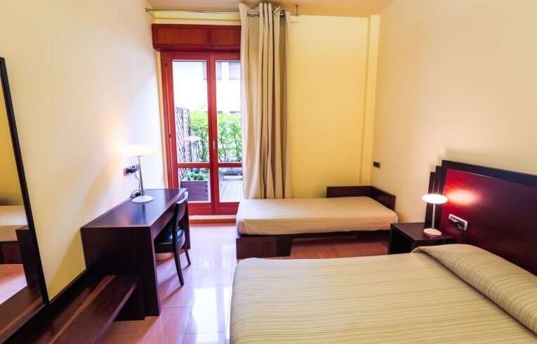 Camera d'hotel con due letti, scrivania e accesso al patio.