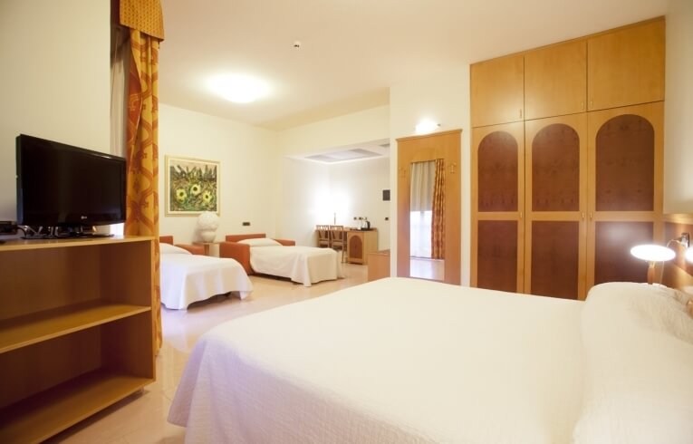 Hotel room featuring multiple beds, a TV, wardrobe, and artwork.
