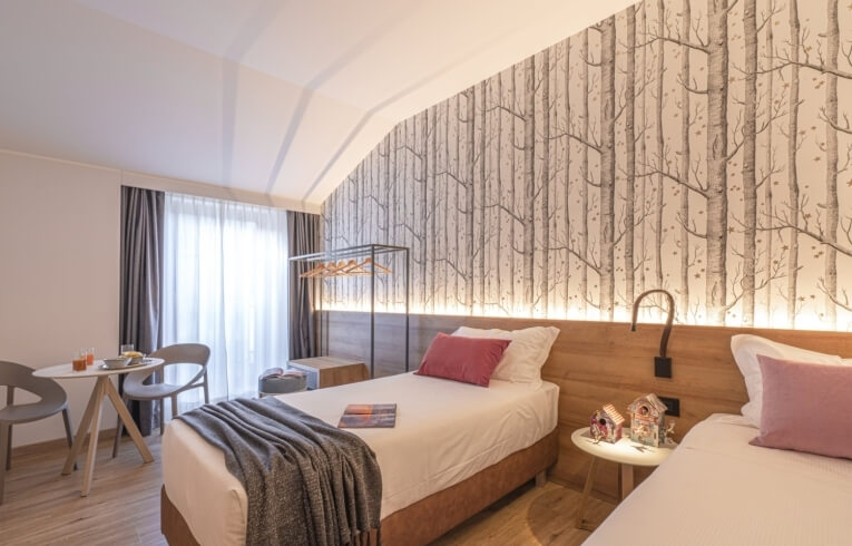 Hotel room with two single beds, tree motif wallpaper, and breakfast tray.