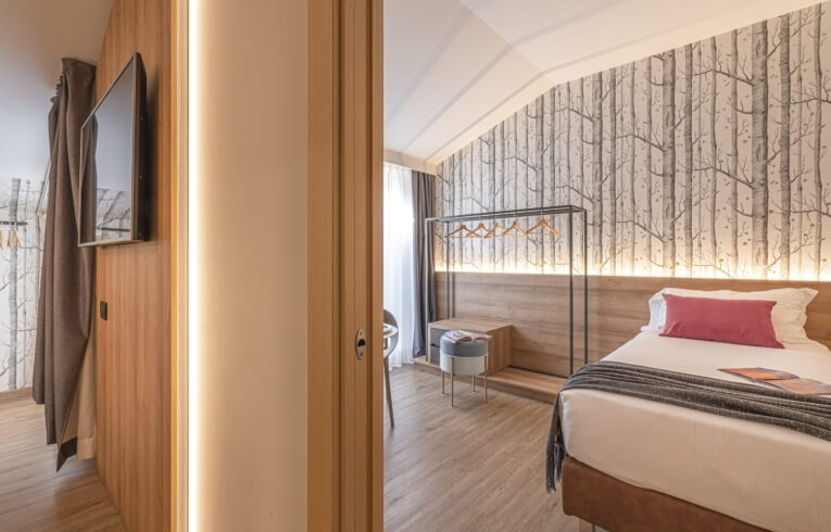 Cozy hotel room with single bed, tree-pattern wallpaper, and wooden furniture.