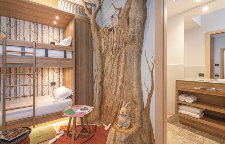 Hotel room with bunk beds, tree sculpture, and bathroom area.