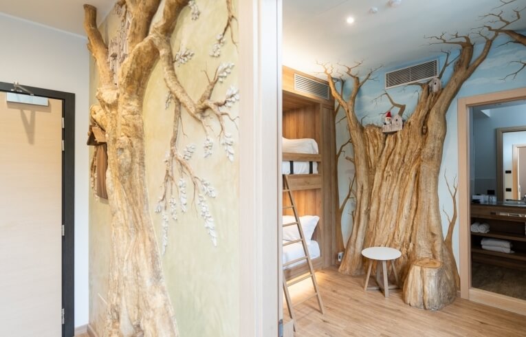 Whimsical hotel room with tree sculpture, bunk beds, and forest mural.