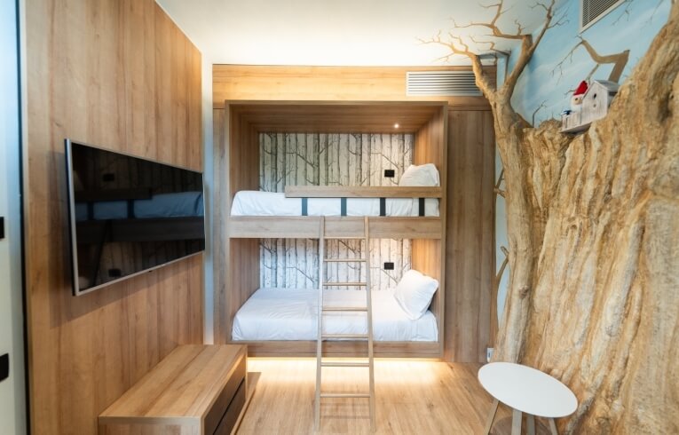 Cozy hotel room with bunk bed, TV, tree trunk decor.