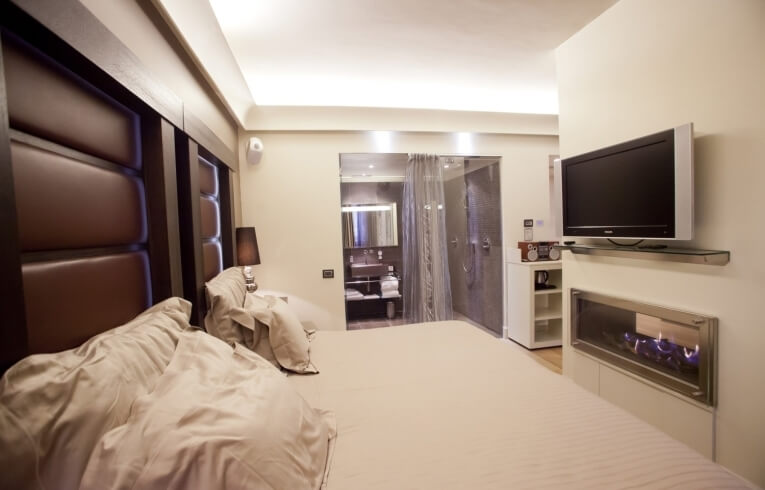 Camera d'hotel con letto grande, TV sopra camino e bagno moderno.