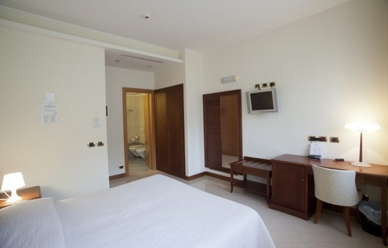 Camera d'hotel con letto, scrivania, bagno e comodino.