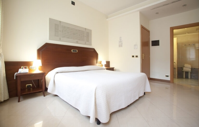 Camera d'hotel con letto, comodino e bagno visibile.