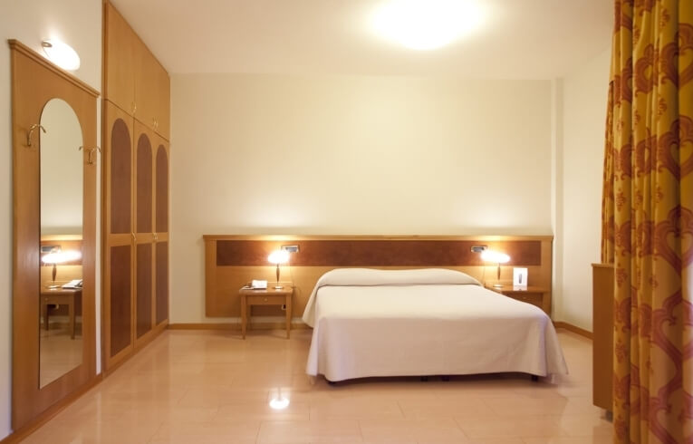 Cozy hotel room with a bed, nightstands, wardrobe, and curtains.