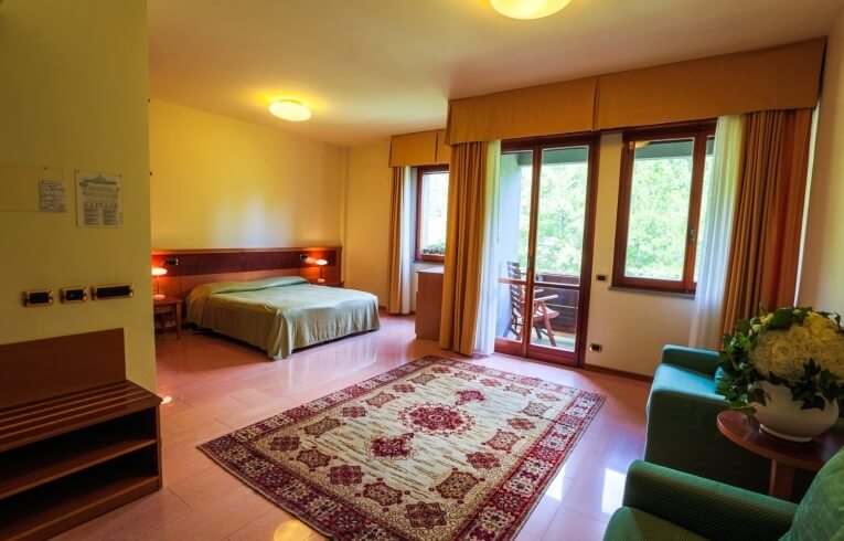 Hotel room with green bedding, balcony, and floral decor.