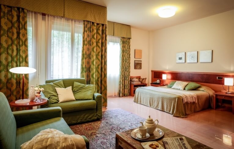 Camera d'hotel con letto grande, divani verdi e set da tè.