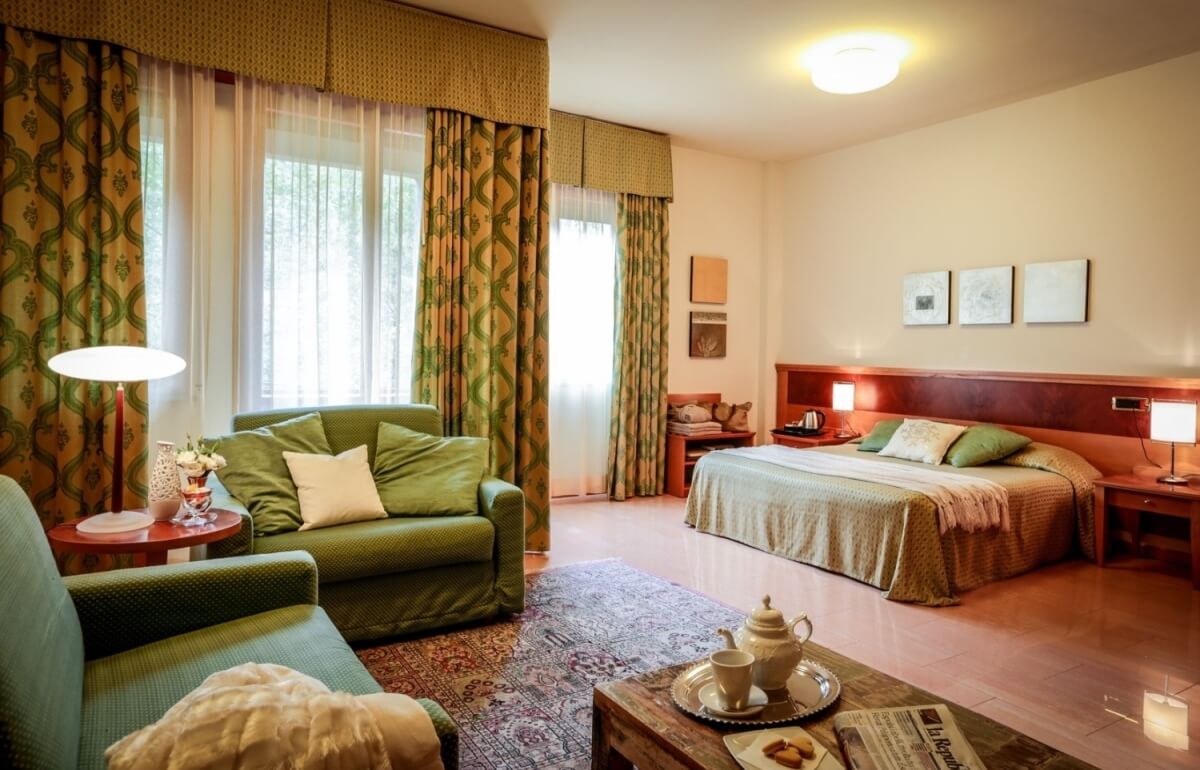 Camera d'hotel con letto, divani, tavolino e tende floreali.