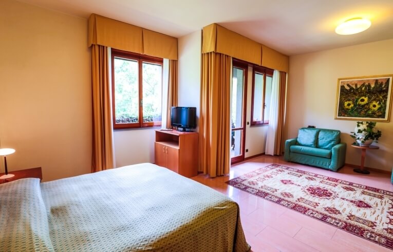 Cozy hotel room with bed, sofa, TV, and sunny decor.