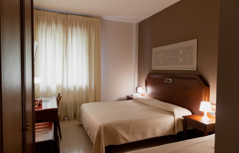 Camera d'hotel con due letti, scrivania e finestra.