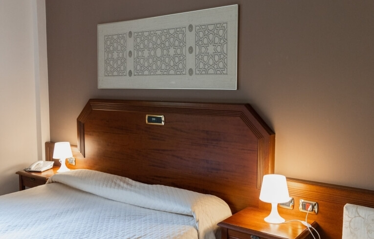 Camera d'hotel con letto, comodini e opere d'arte geometriche.